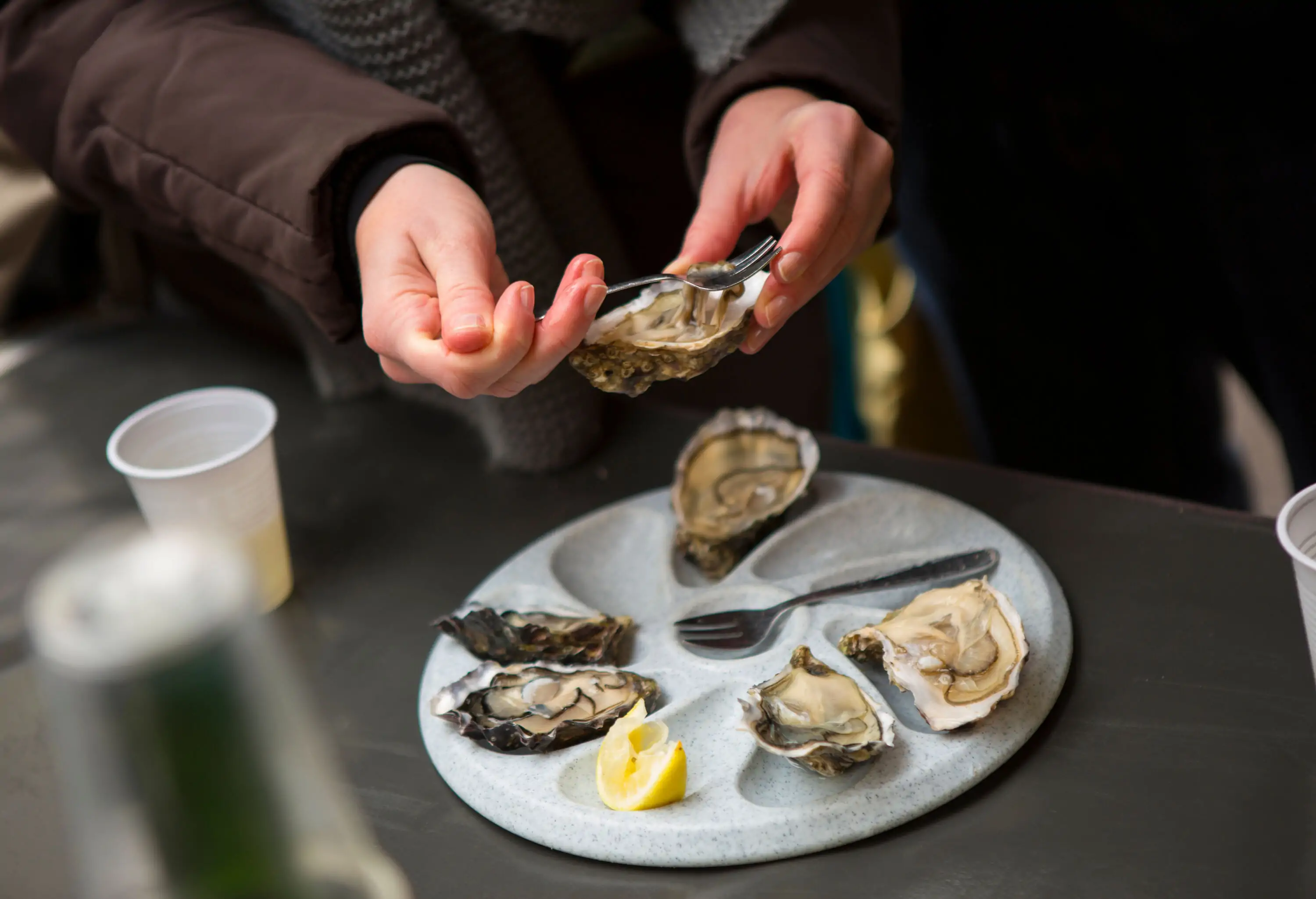 A person using a fork to remove an oyster from its half-shell.