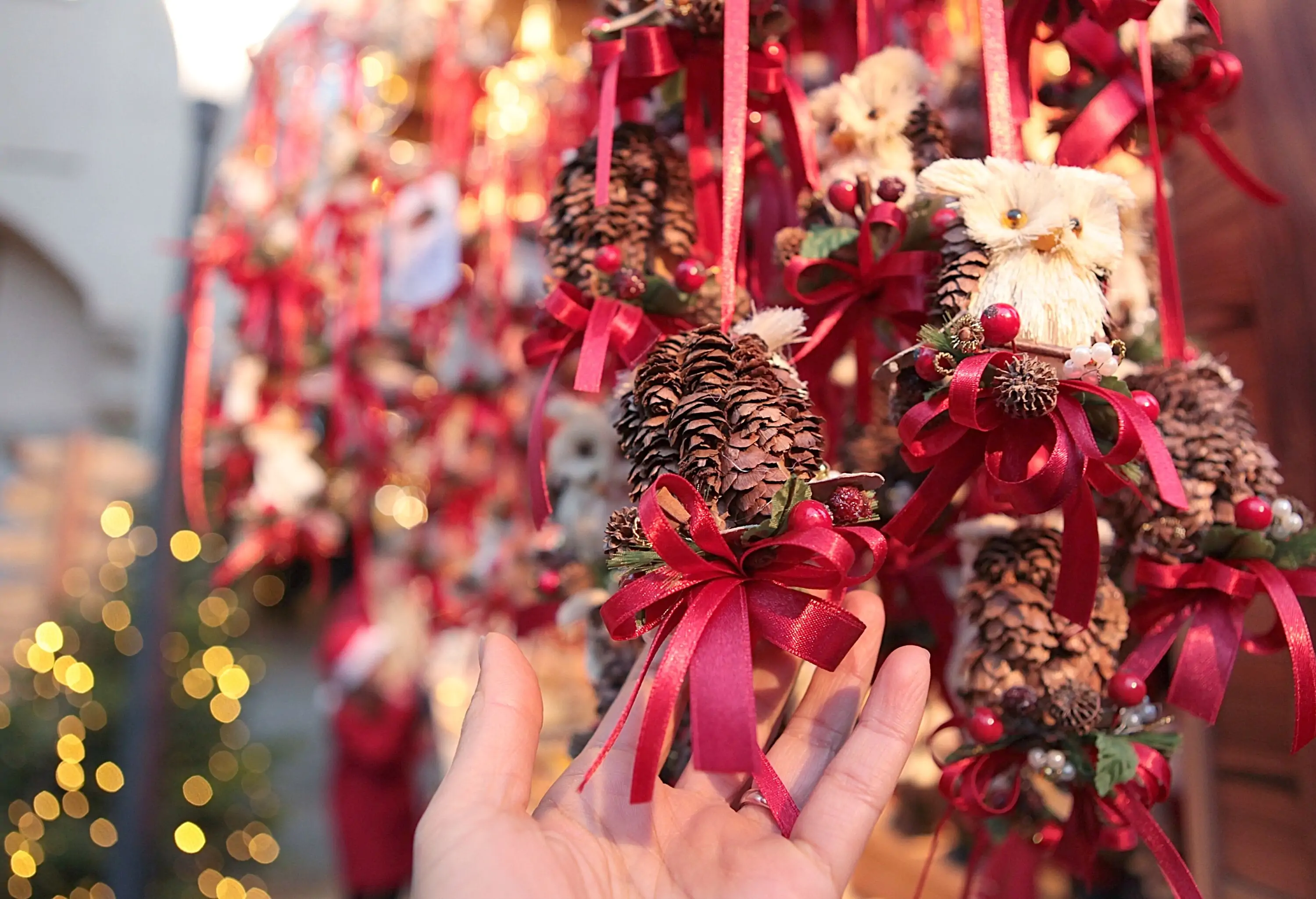 A hand holding a pinecone with a red ribbon.