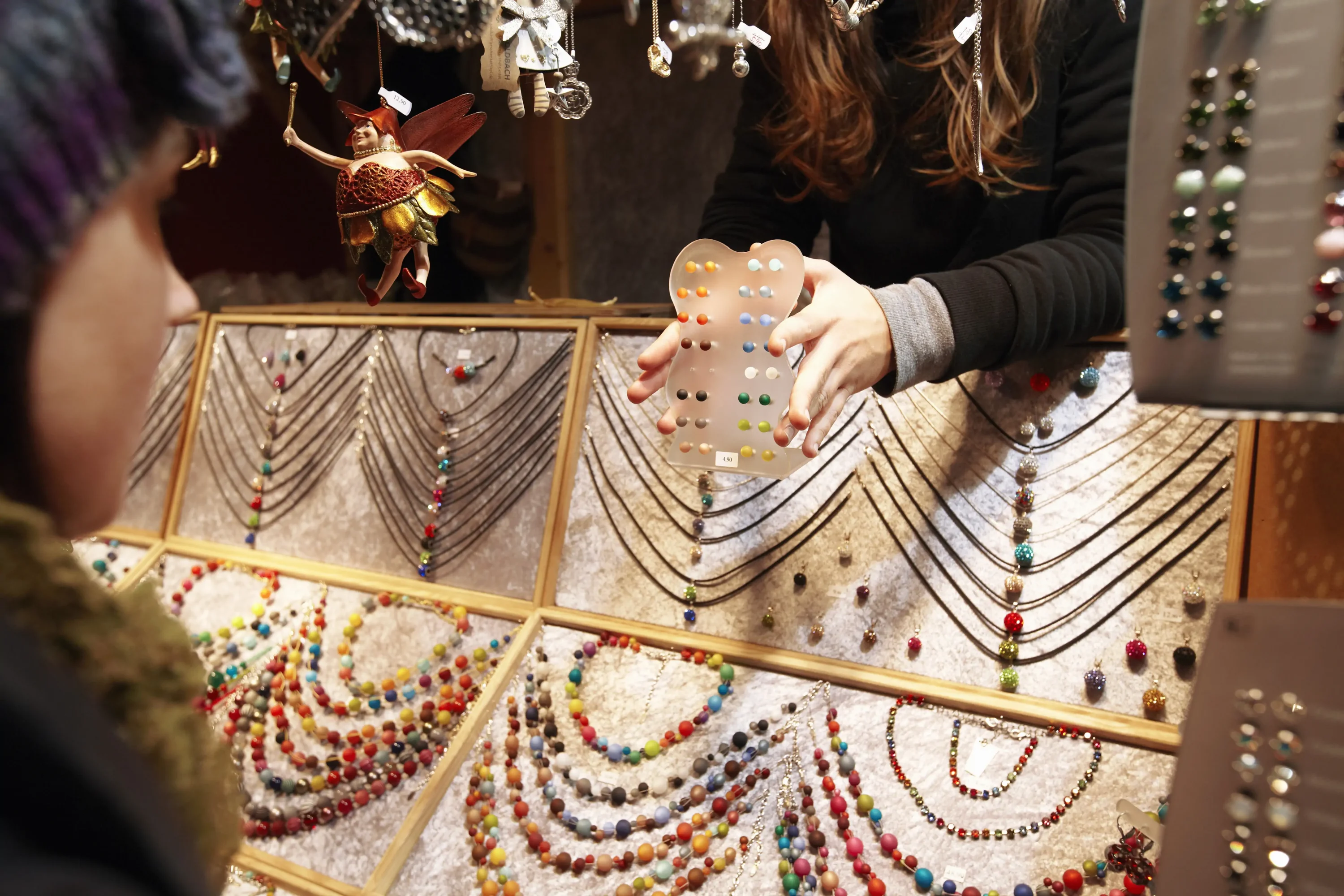 Hands holding a selection of jewellery earrings in a shop with a display of colourful necklaces.