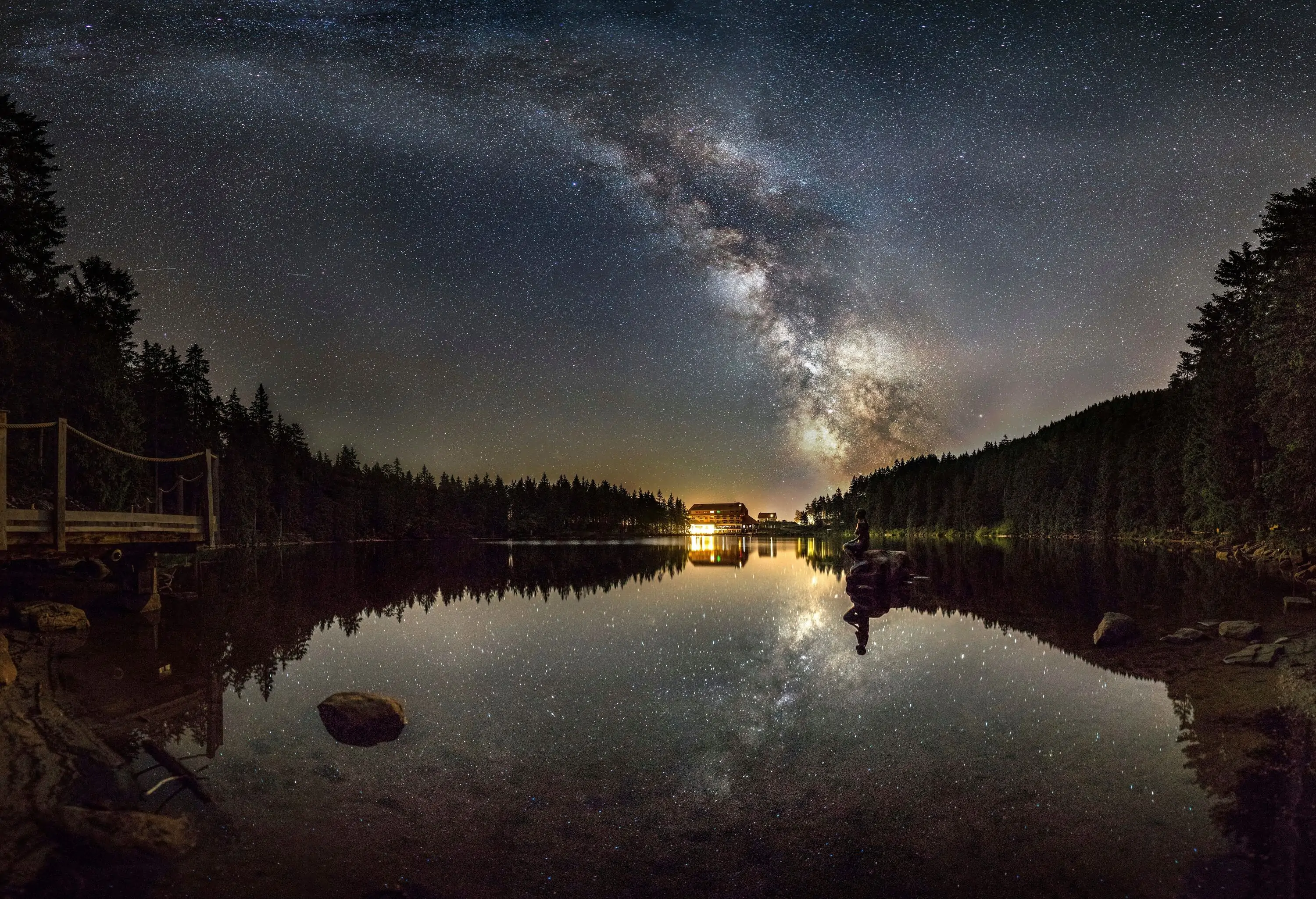 A lake reflecting the trees around it and the night sky littered with stars.