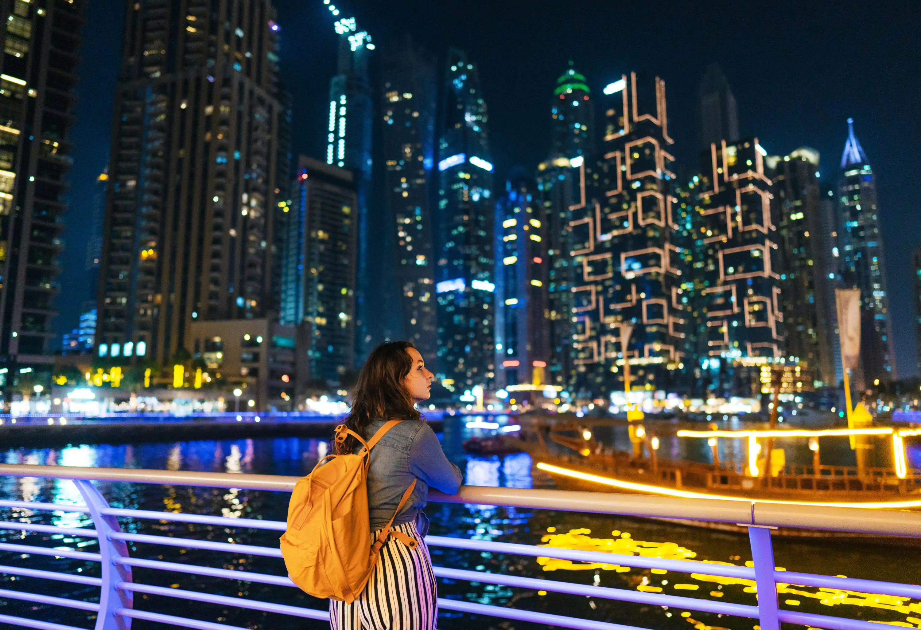 Young Caucasian woman gazing at Dubai Marina at night, tall buildings in the background