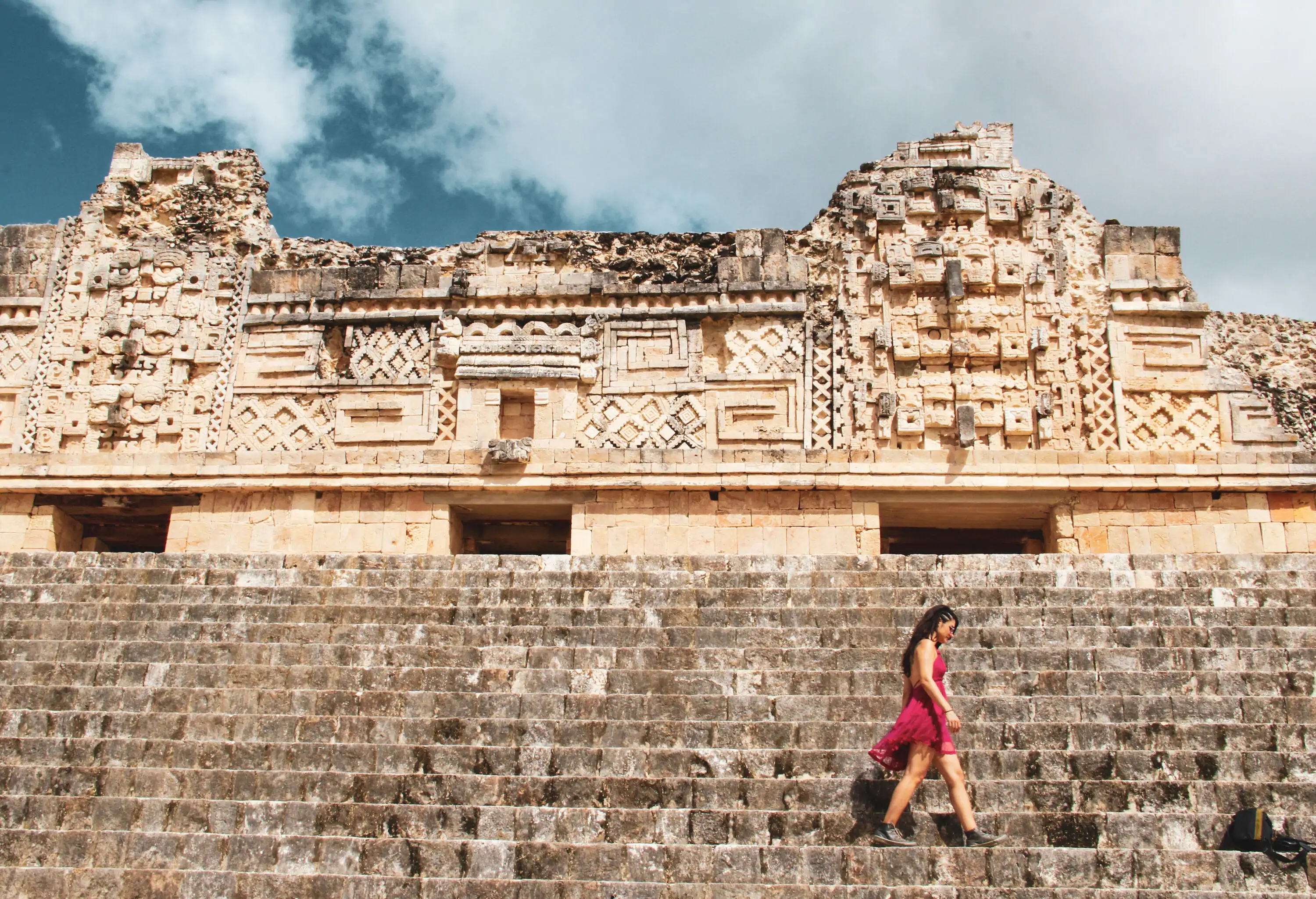 A woman is walking on a staircase with ruins of an ornate wall.