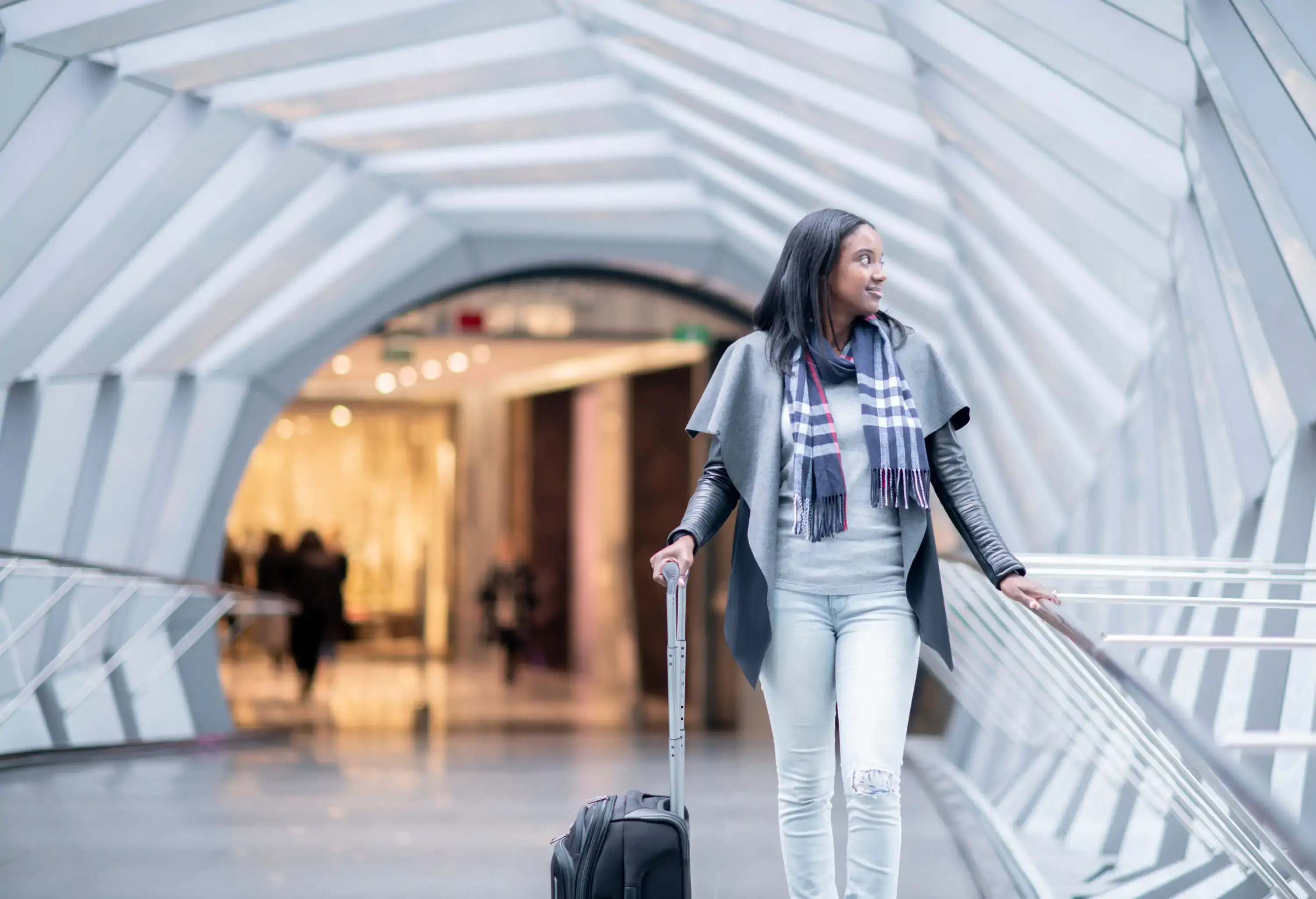 A woman of African descent is walking through an airport carrying a suitcase and looking around