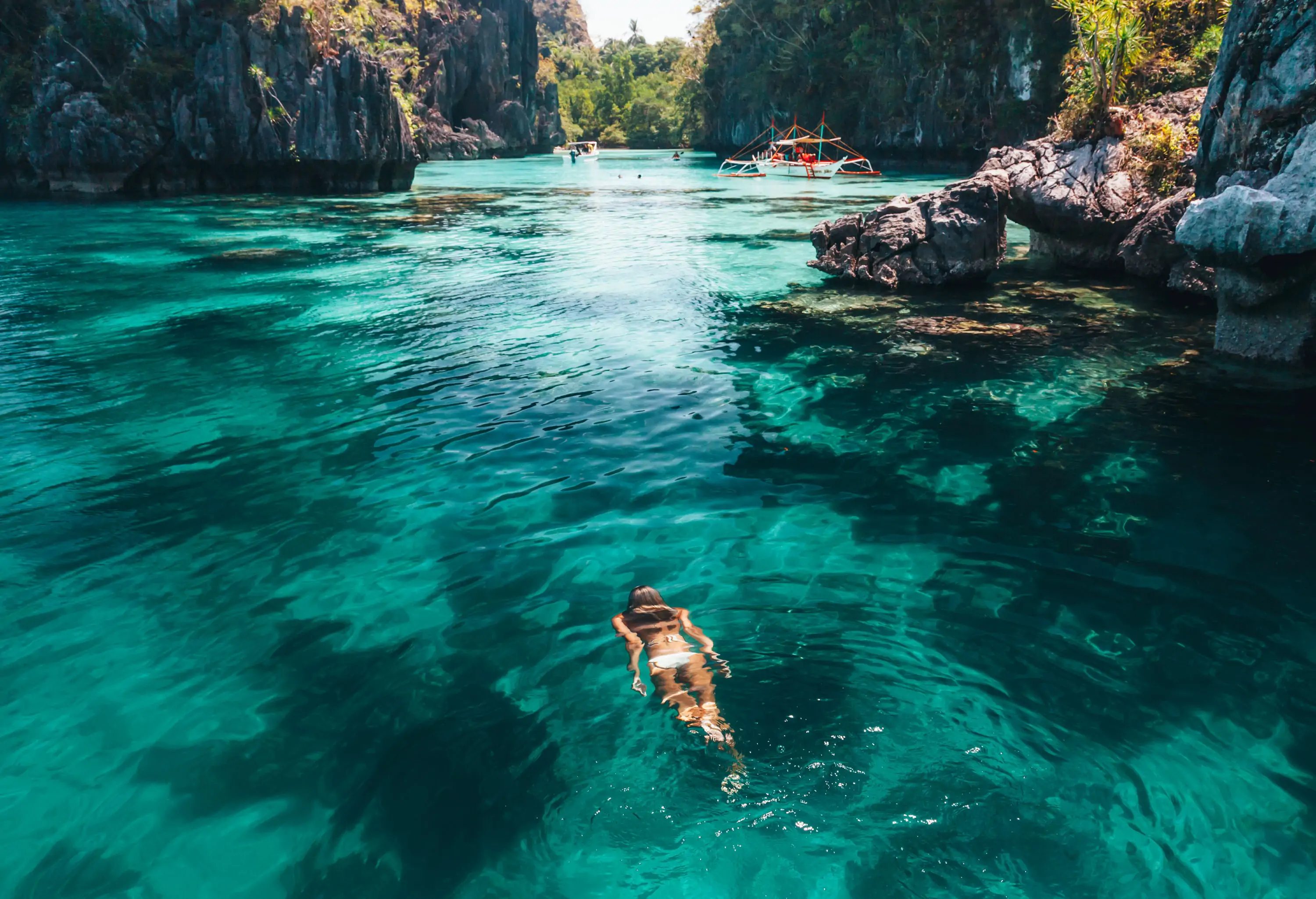 A woman swims in the clear water lagoon surrounded by towering stone formations.