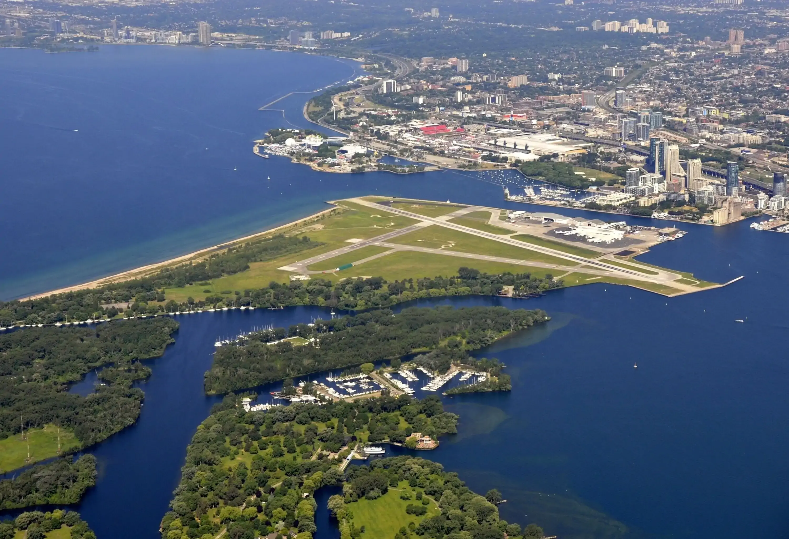 An airport runway on an island between a forested area and a cityscape beside a lake.