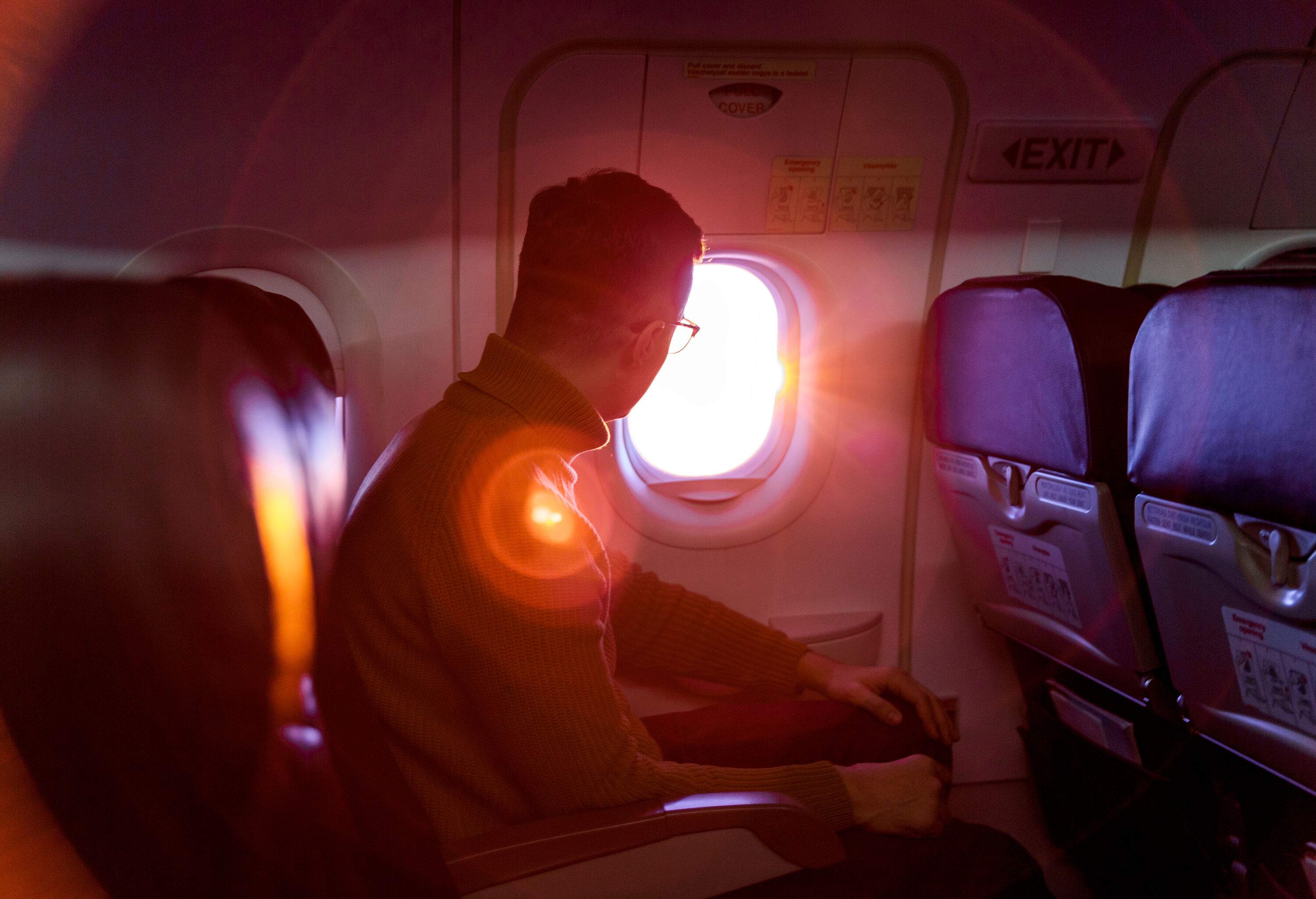 A man seated inside an aircraft looks at the scenic sunset through the window.