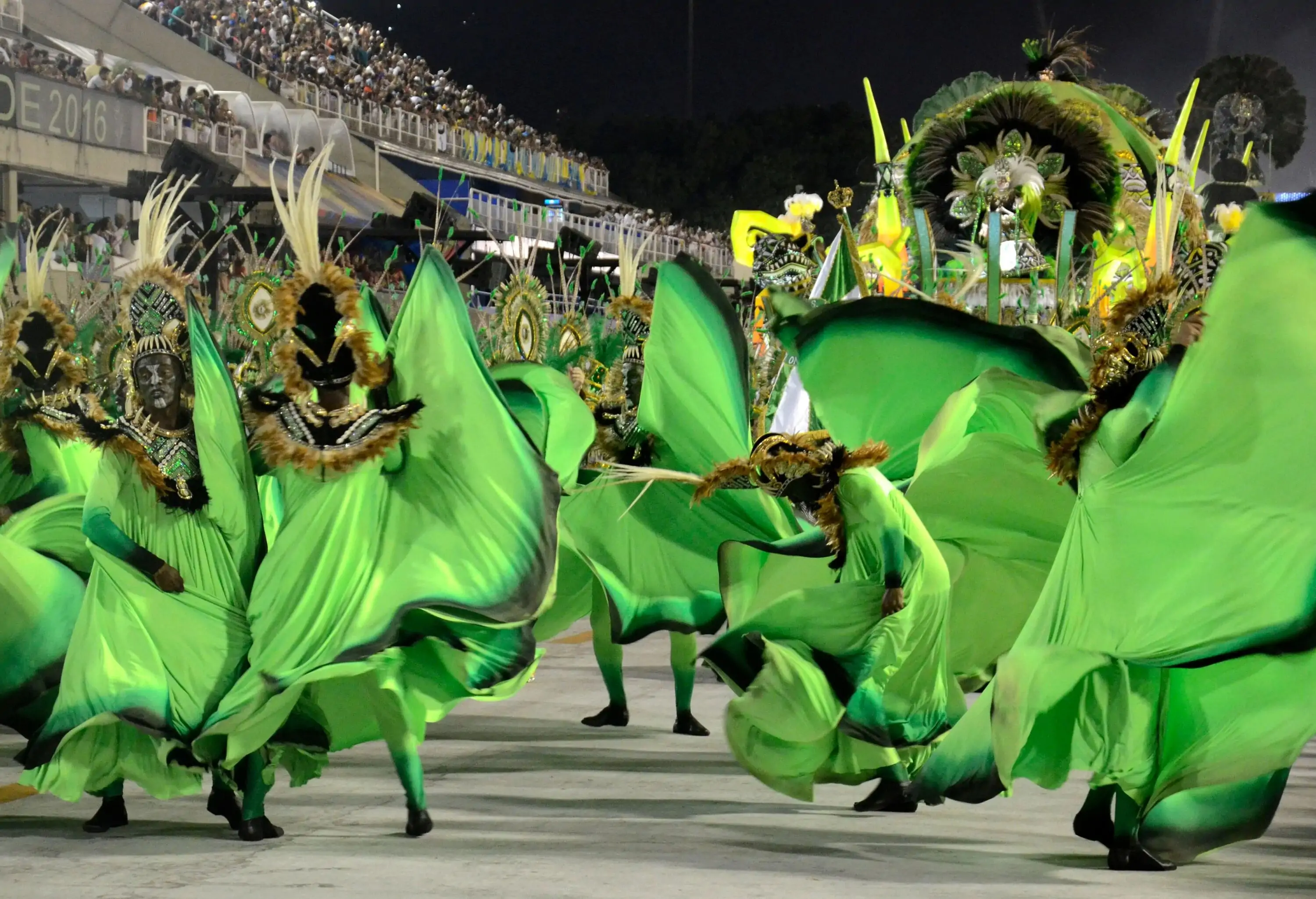 Performers in vibrant green costumes dance in the centre with a captivating crowd watching with excitement and joy.