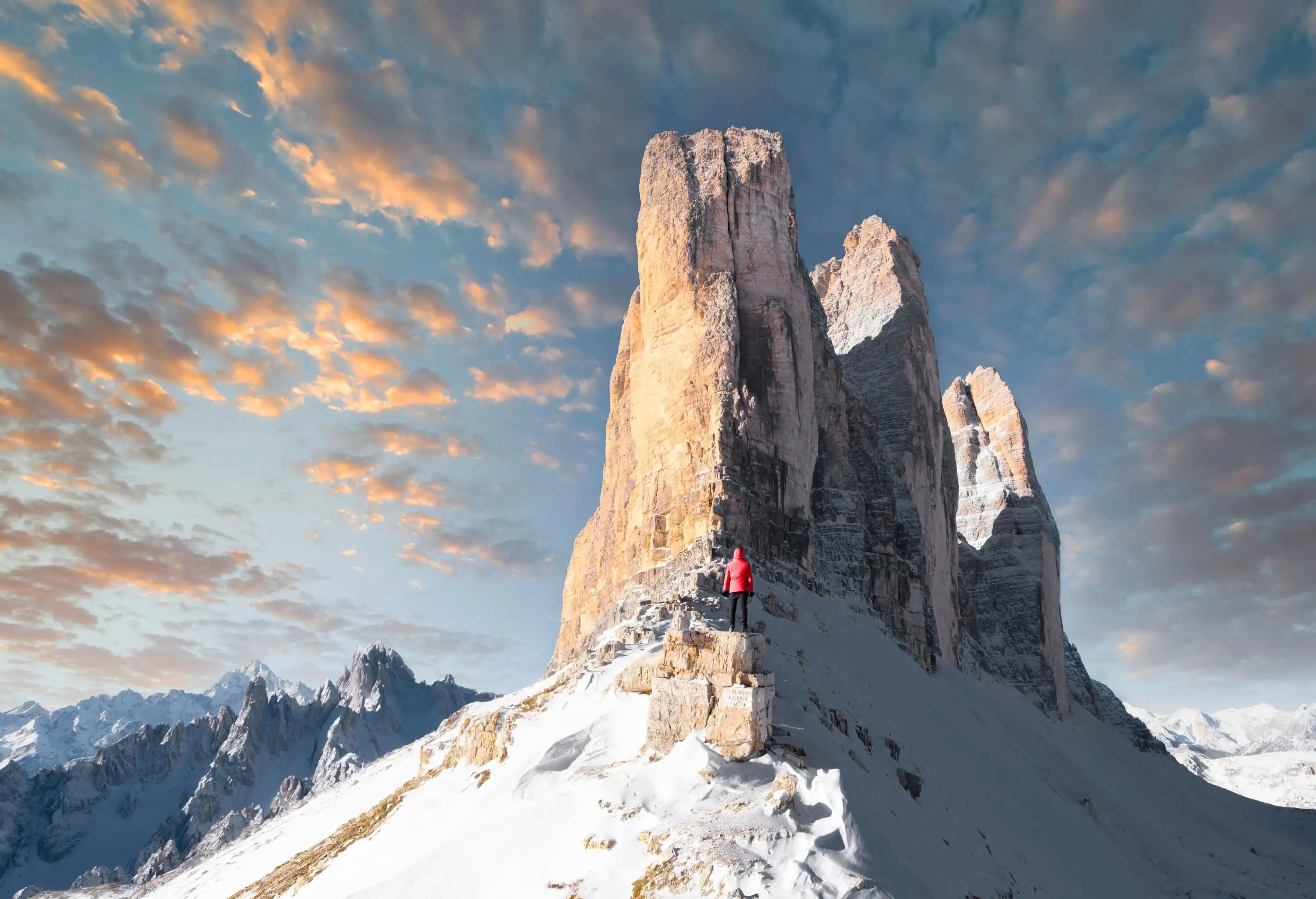 Woman in a red hooded jacket standing on a rock, staring up at an enormous dolostone formation.