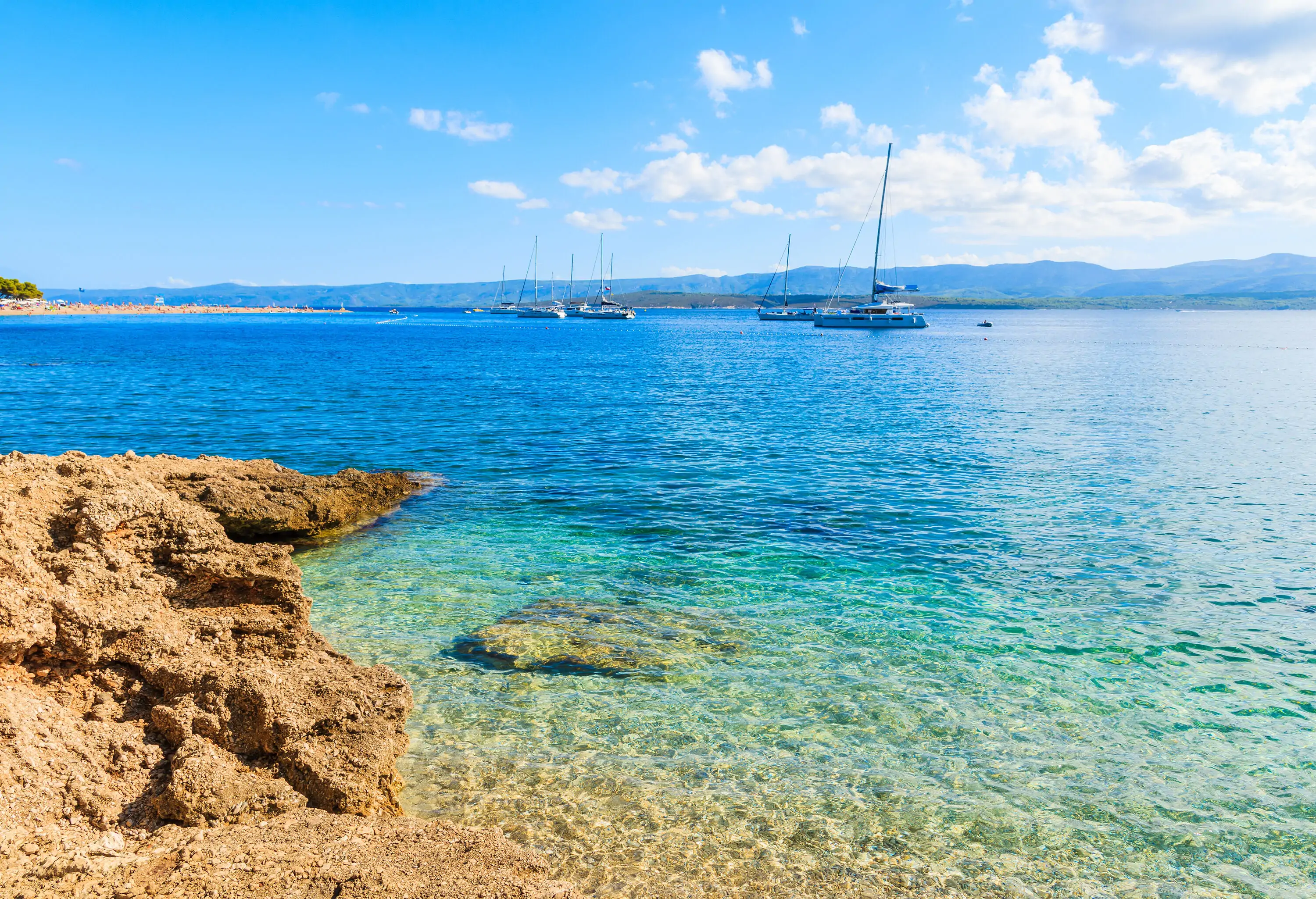 A clear water beach with a rocky shore against the cloudy blue sky.