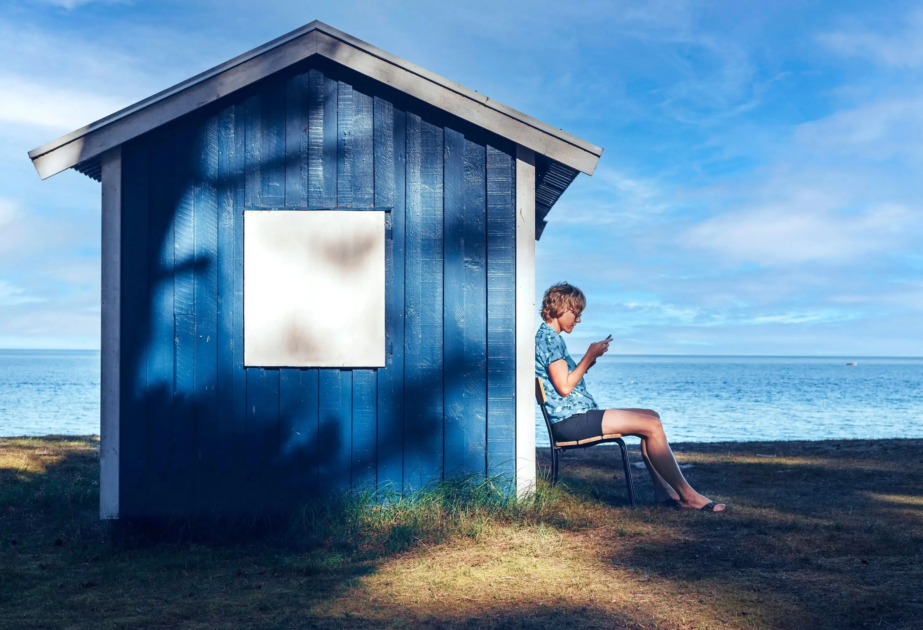 Discover Ähus: Hidden Gem in Sweden's Skåne Region. Women sitting with her back to a small blue cottage.