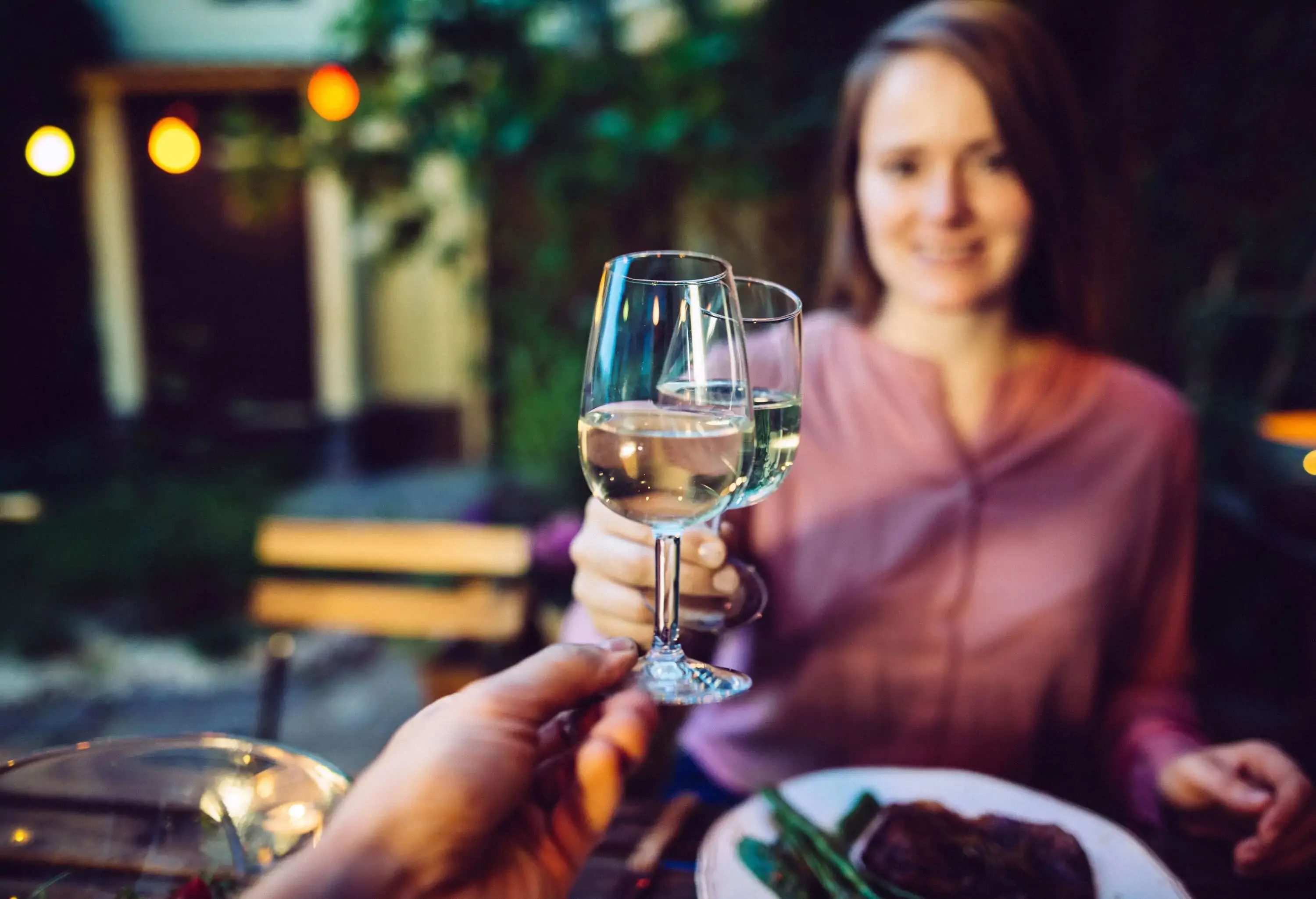 A woman gives a toss of wine glasses while having dinner.