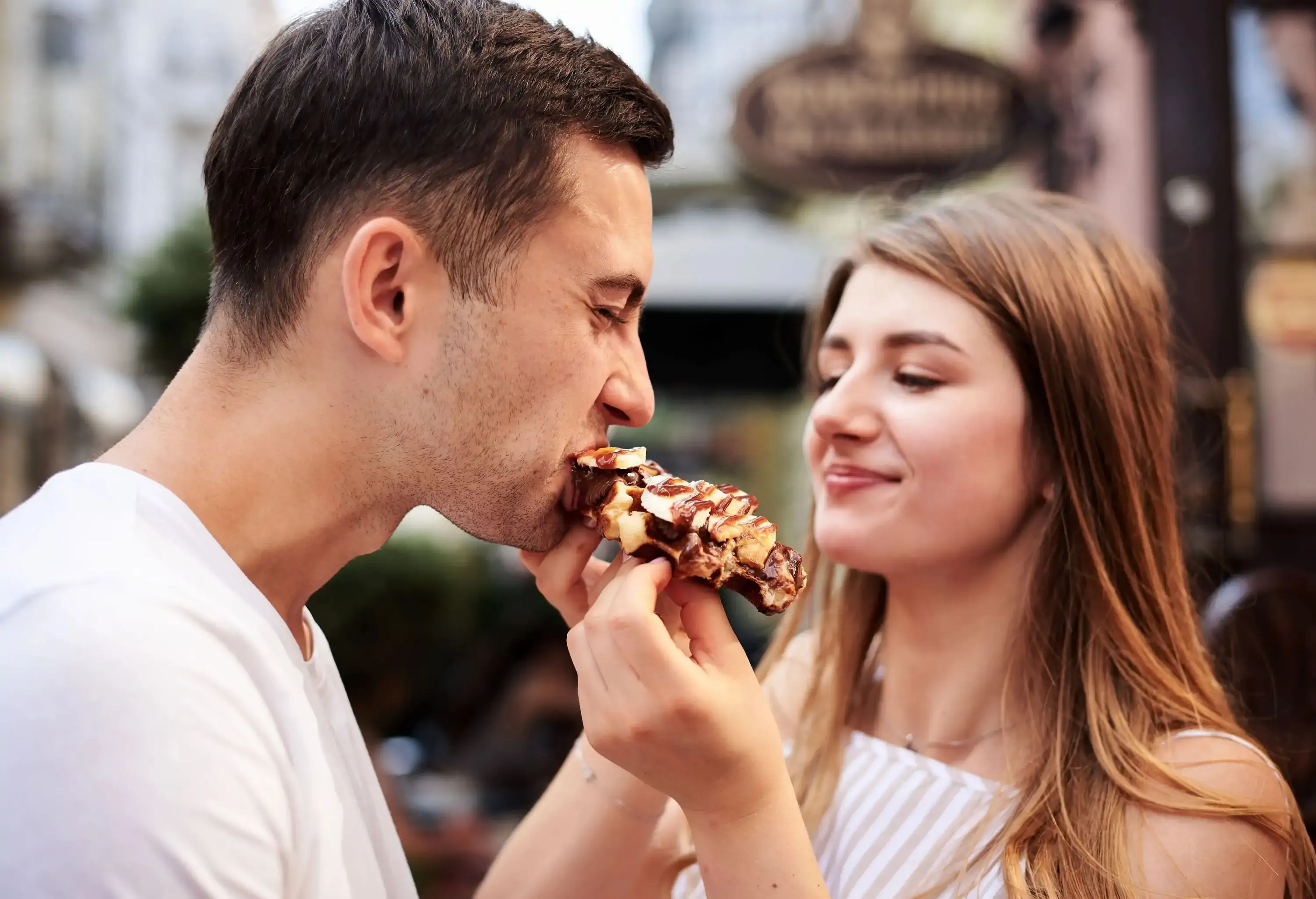 A brunette woman feeds a man with a chocolate waffle.