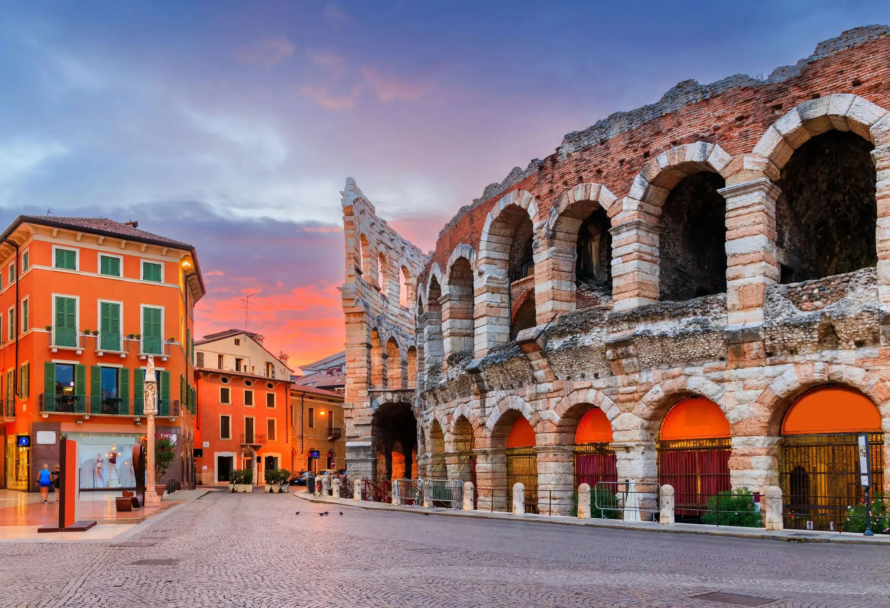 A cobbled street lined with classic buildings and an arched and curved facade of a Roman amphitheatre.