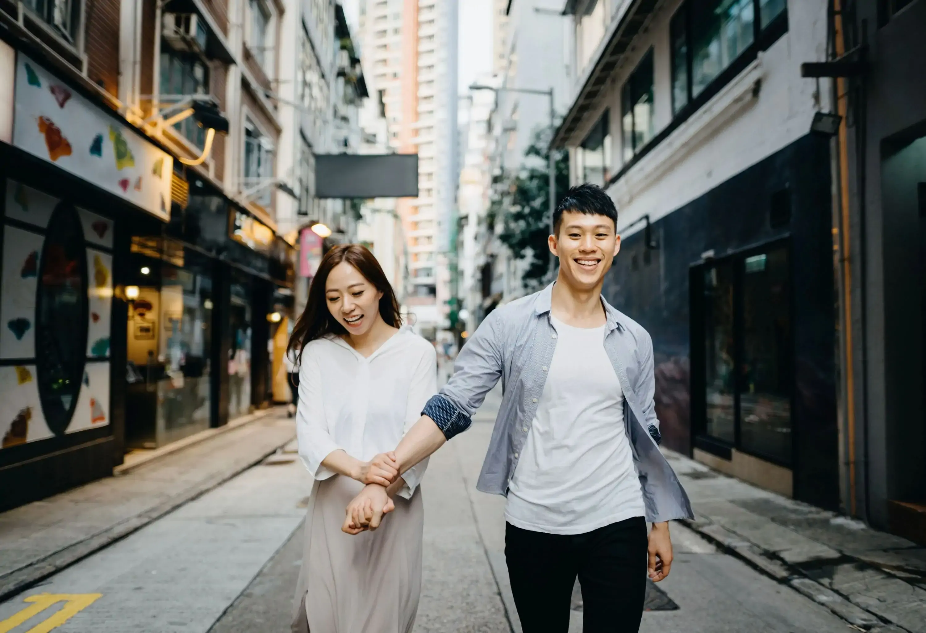 Young Asian couple holding hands and smiling as they walk through local city street in Hong Kong