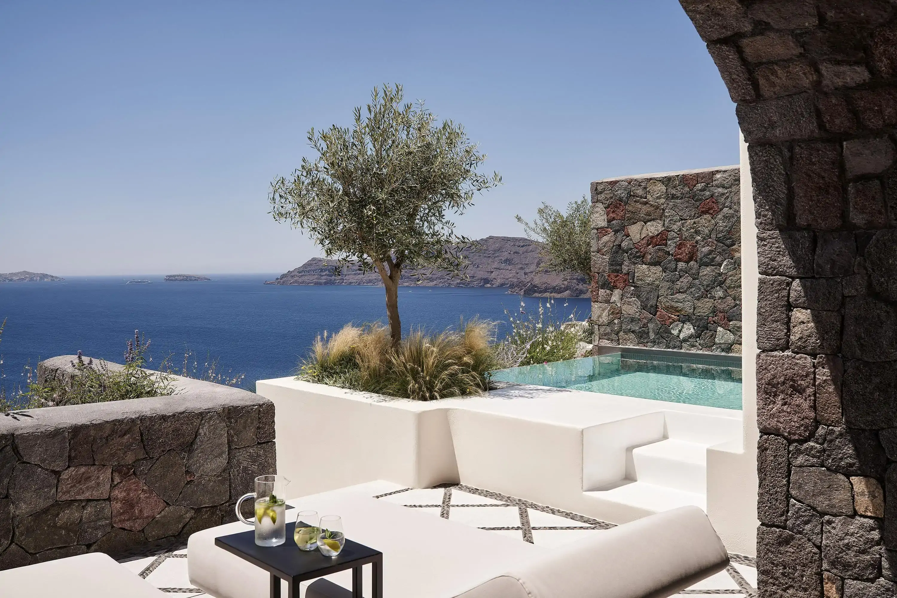 Private patio with modern garden furniture and private splash pool by an olive tree overlooking a Mediterranean island