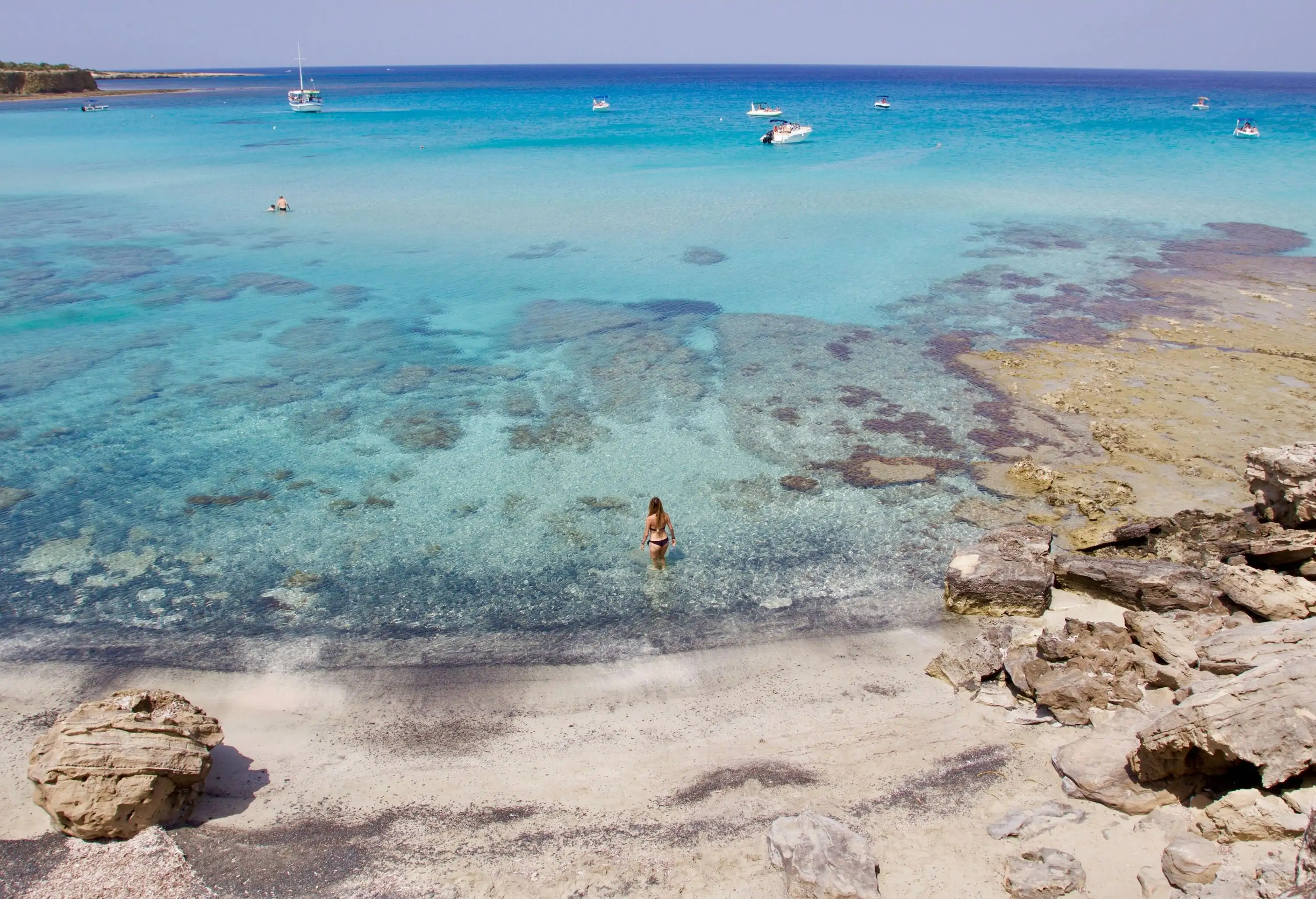 A captivating view of a stunning blue lagoon bay with crystal clear and turquoise water dotted with white boats and people swimming.