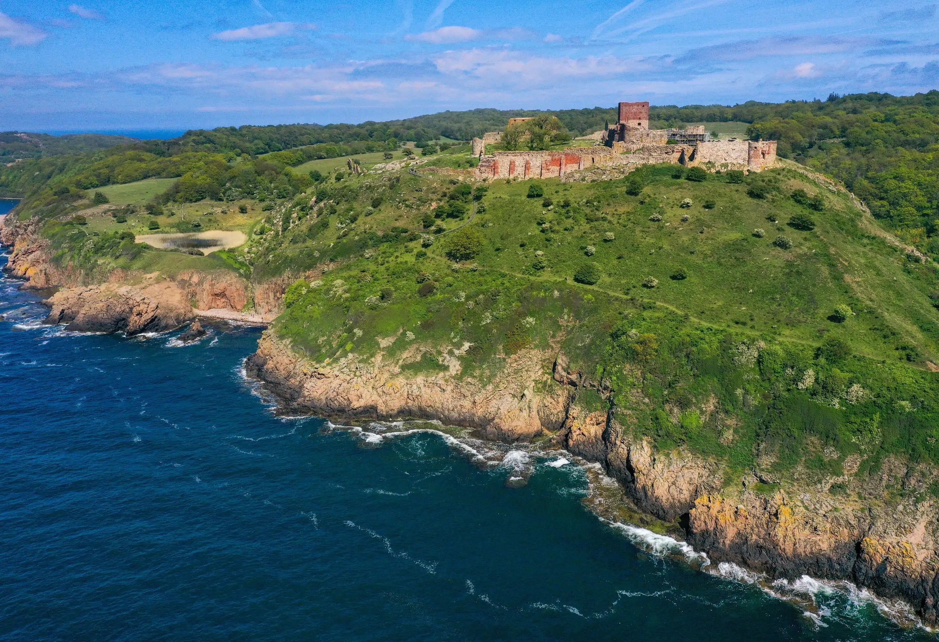 Ruins of a fortress perched atop a forested rocky island, majestically surrounded by the azure sea.