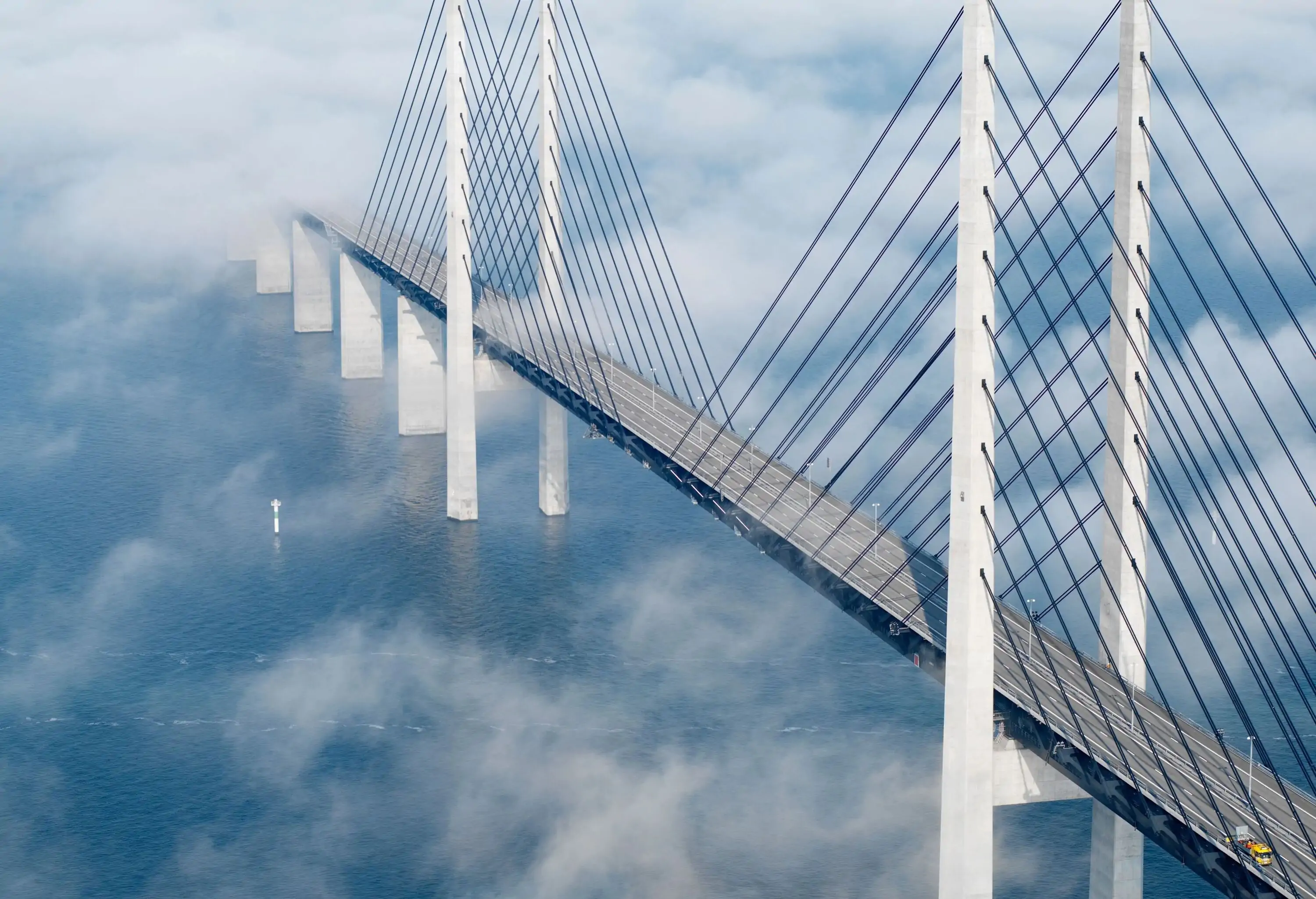 A cable-stayed motorway bridge surrounded by mist rising in the air.