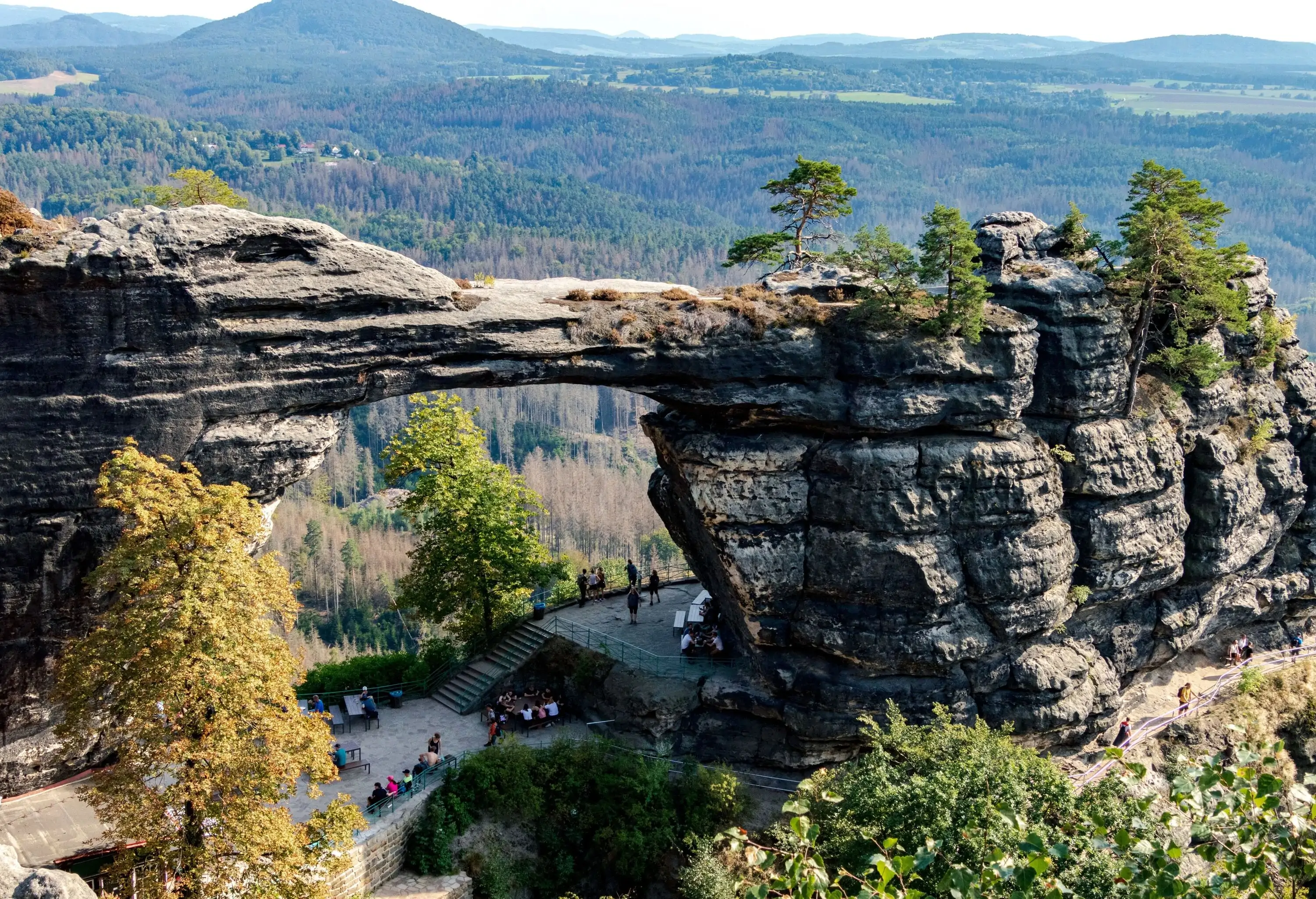 The Pravčická Archway, a natural wonder set amidst a picturesque wooded landscape, is visited by people seeking its natural beauty.