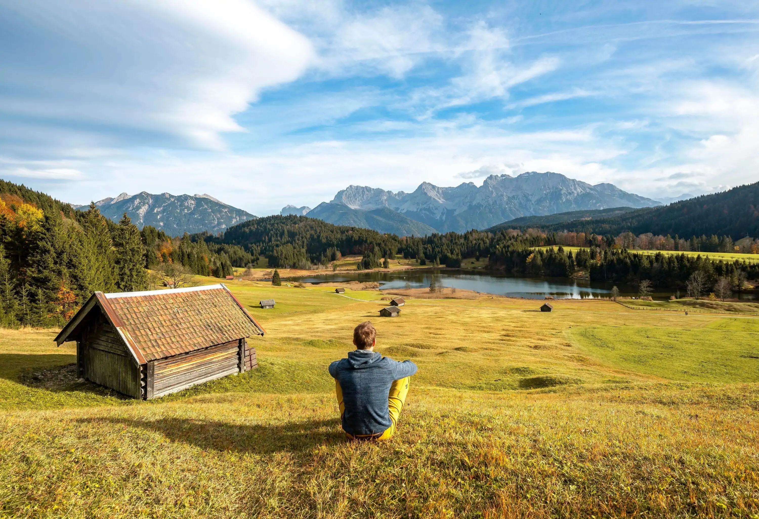 A man sitting on the grass looking far ahead into the lake and mountains.