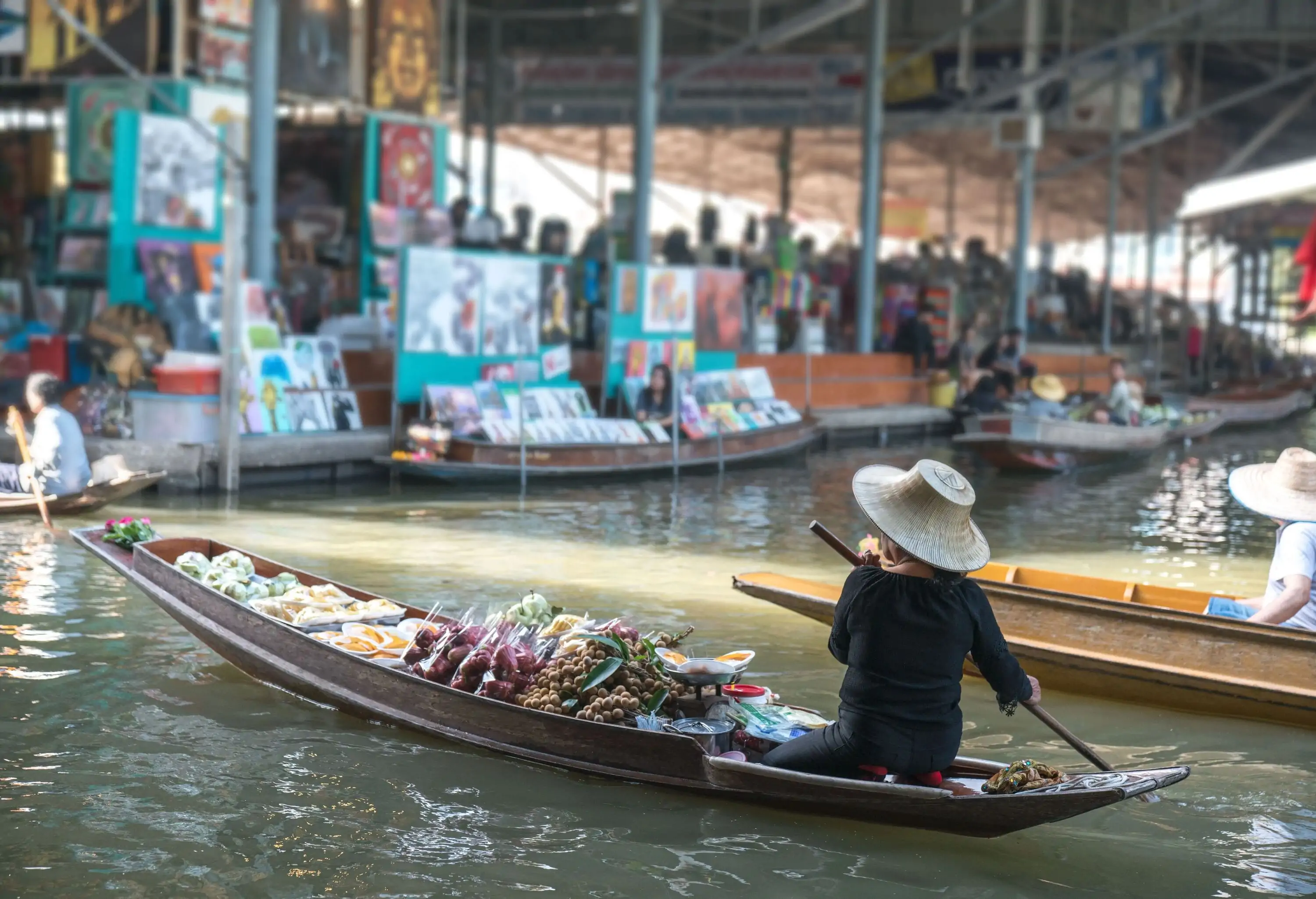 A woman wearing a straw hat paddling a boat laden with delicacies across the river.