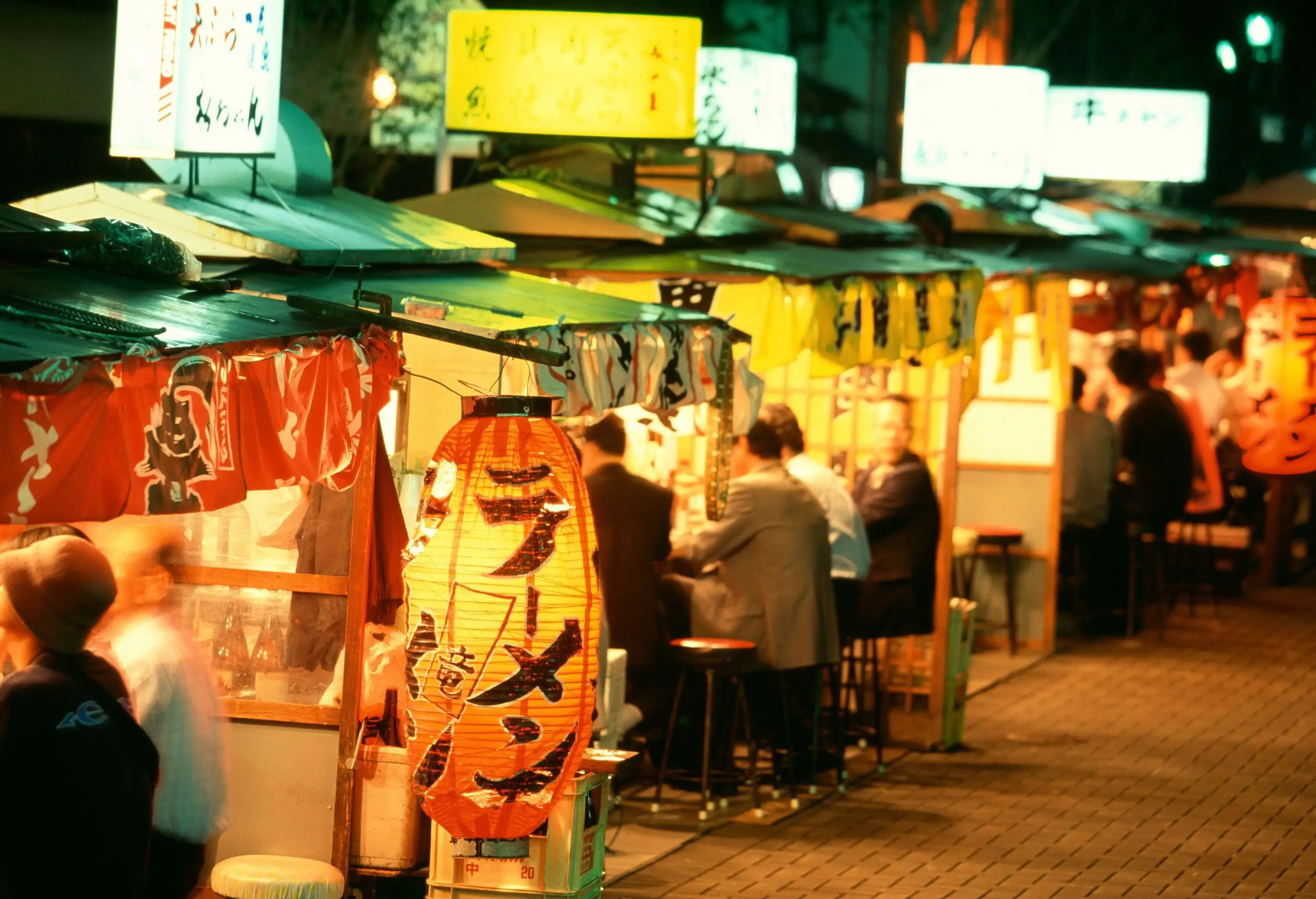 People dine inside street restaurants illuminated by bright advertisement signages.