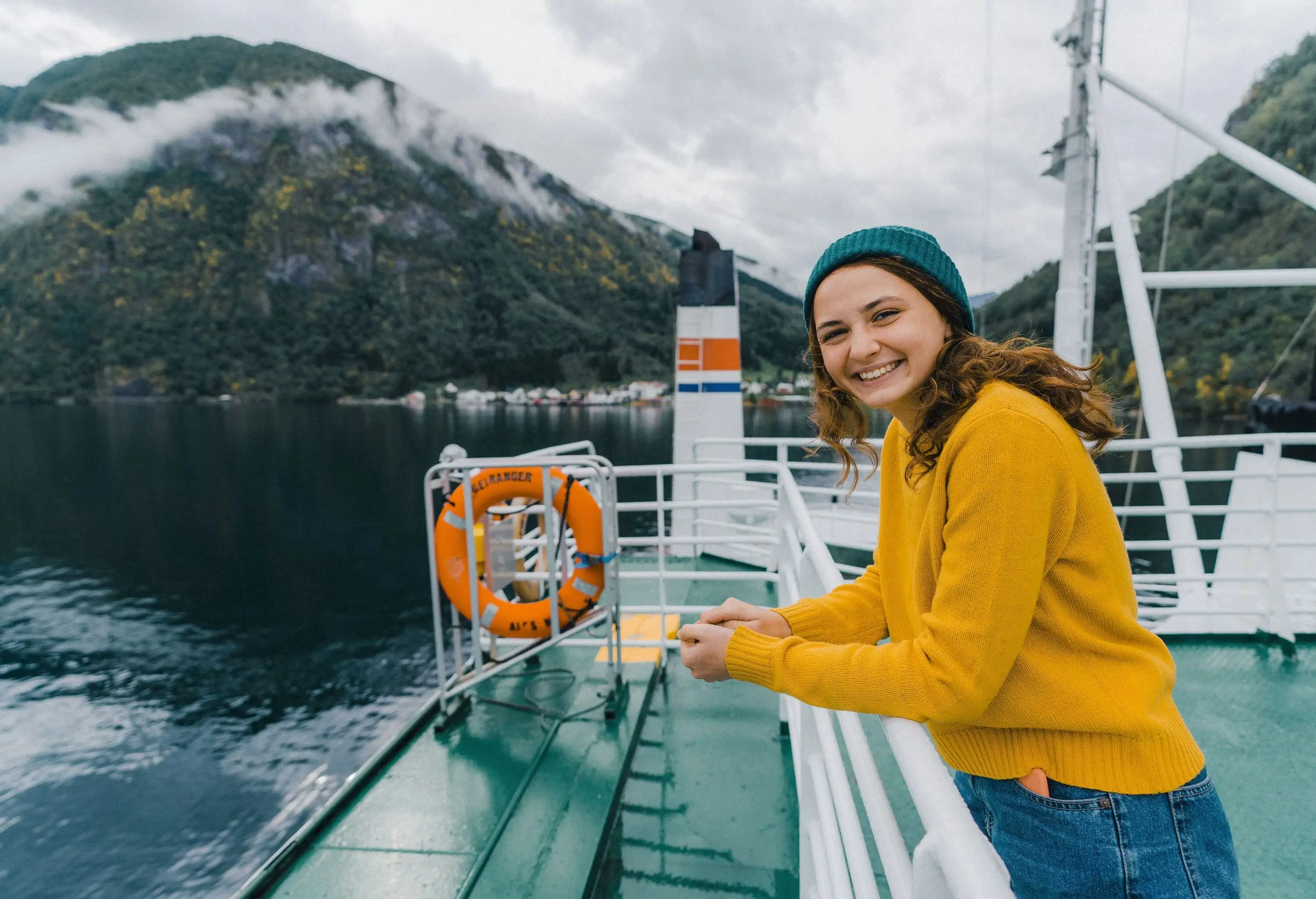 A woman in a yellow sweater smiling as she leans on the railing of a boat's deck.